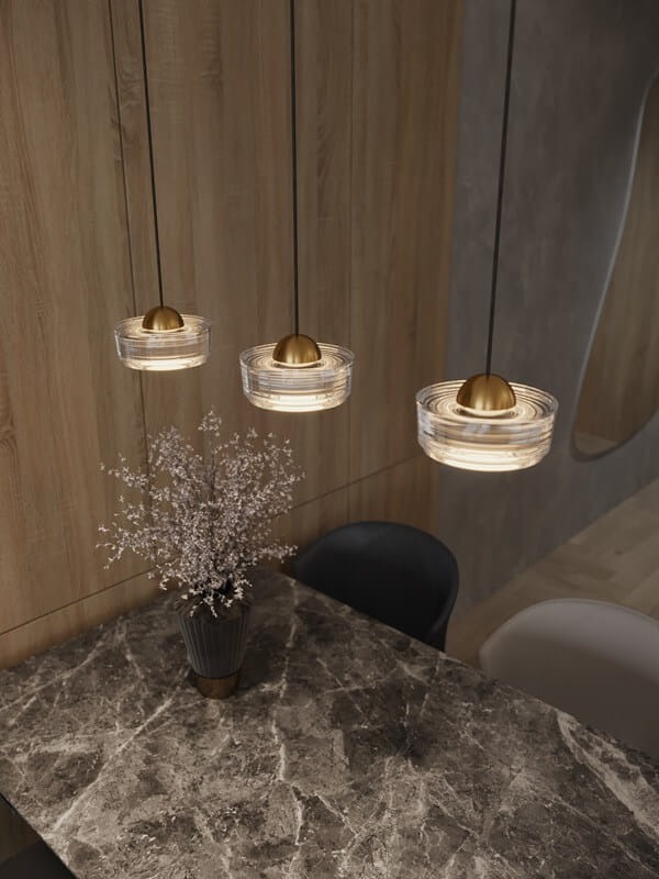 Lampa wisząca Lipari z trzema źródłami LED 22W w kolorze białym. Szklane klosze w formie okrągłych misek z metalowymi, złotymi elementami, zawieszone na cienkich linkach. W tle widoczny stół z marmurowym blatem i wazon z kwiatami.