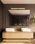 Kinkiet Fayette 1xLED 18W w kolorze złotym, zamontowany nad podwójną umywalką w nowoczesnej łazience. Oświetlenie w stylu minimalistycznym, IP44, umieszczone na ciemnej ścianie, w towarzystwie lustra i drewnianych mebli.