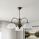 Żyrandol Delos 3xE27 w kolorze patyny z trzema białymi, półkulistymi kloszami. Umożliwia zamontowanie trzech żarówek. Produkt wiszący, z klasycznym designem, umieszczony na tle jasnego pomieszczenia z obrazem w tle.
