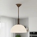 Lampa wisząca Delos D30 z metalowym stelażem w kolorze patyny. Szklany klosz w kształcie półkuli w białym kolorze. Produkt zawieszony na długim, prostym uchwycie, w aranżacji z jasnym tłem i elementami wyposażenia wnętrza.