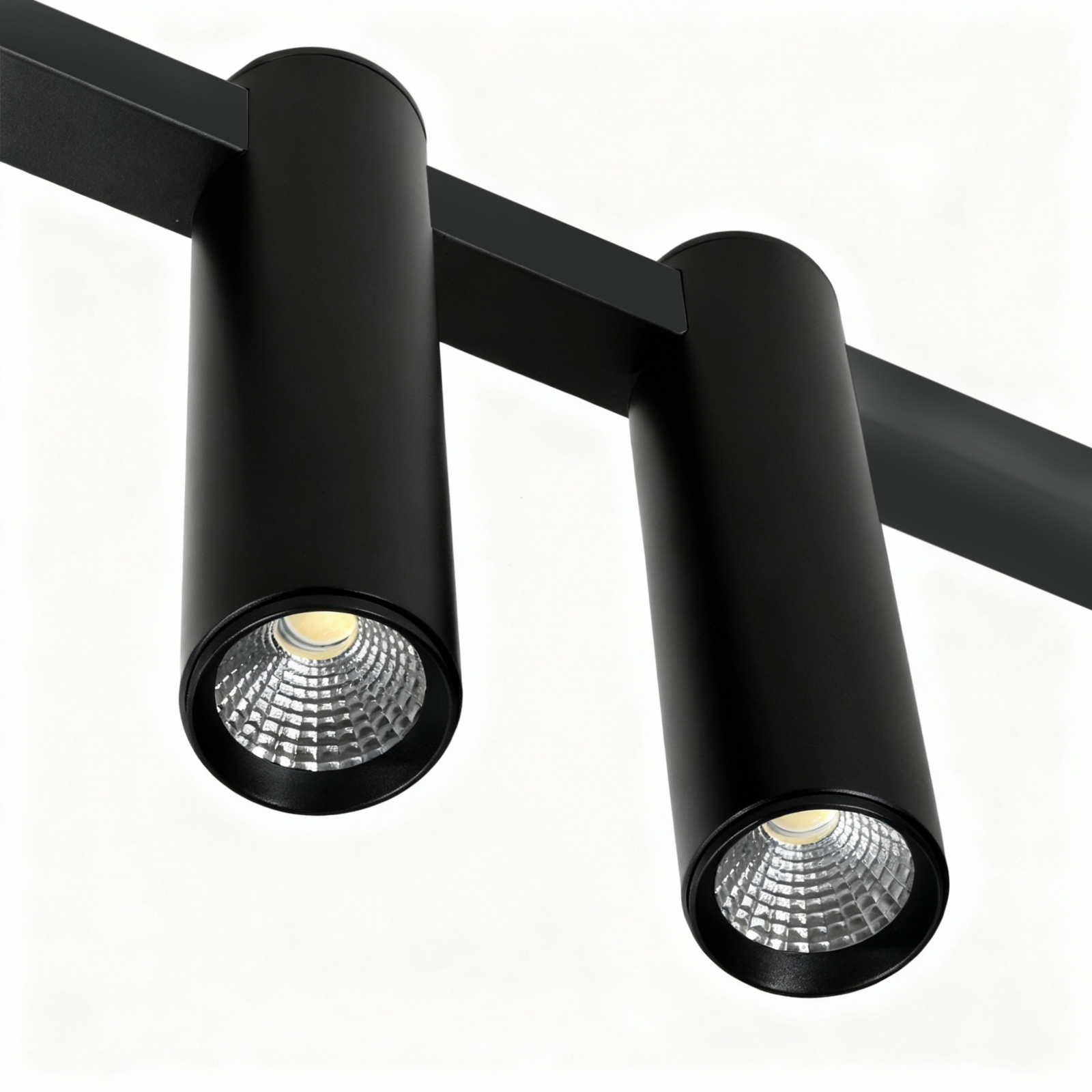 Lampa wisząca Kona z czterema punktami LED, 30W, w kolorze czarnym. Okrągłe oprawy z wyraźnym wzorem soczewki, zamontowane na prostokątnej belce. Kąt ujęcia zbliżeniowy, ukazujący detale konstrukcji.