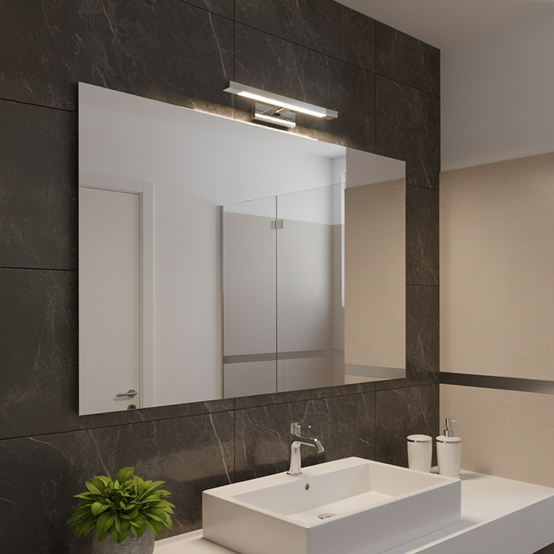 Kinkiet Klimt L40 LED 8W CCT IP44 w chromowanej obudowie, zamontowany nad lustrem w nowoczesnej łazience. Oświetlenie skierowane w dół, na tle ciemno-skalnej ściany. W zestawie widoczny umywalka i roślina w doniczce.