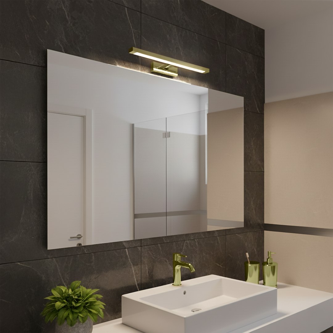 Kinkiet Klimt L40 LED 8W CCT IP44 w kolorze złotym, zamontowany nad lustrem w nowoczesnej łazience. Oświetlenie w kształcie prostokąta, z metalowym wykończeniem, na tle ciemnej, marmurowej ściany.
