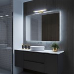 Kinkiet Klimt L40 LED 8W CCT IP44 w kolorze złotym, zamontowany nad lustrem. Oświetlenie ma prosty, nowoczesny design z metalowym wykończeniem, emitującym ciepłe światło. Widoczna aranżacja łazienki z umywalką i rośliną w doniczce.