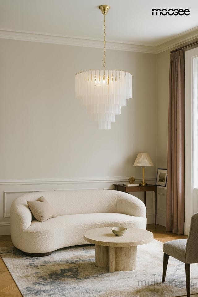 Lampa wisząca Gordon 60, z 12 miejscami na żarówki E14, w złotej oprawie. Charakteryzuje się kryształowym kloszem w formie schodkowej, zawieszona na złotym łańcuchu. Umieszczona w eleganckim wnętrzu z jasnymi ścianami i nowoczesnymi meblami.