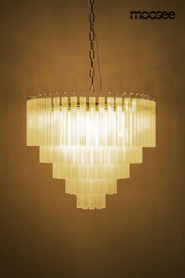 Lampa wisząca Gordon 80 z 21 gniazdami E14, w kolorze złotym. Posiada szereg prostokątnych, transparentnych kloszy ułożonych w kształcie stożka. Zawieszona na łańcuchu, emitująca ciepłe światło na tle jednolitej ściany.