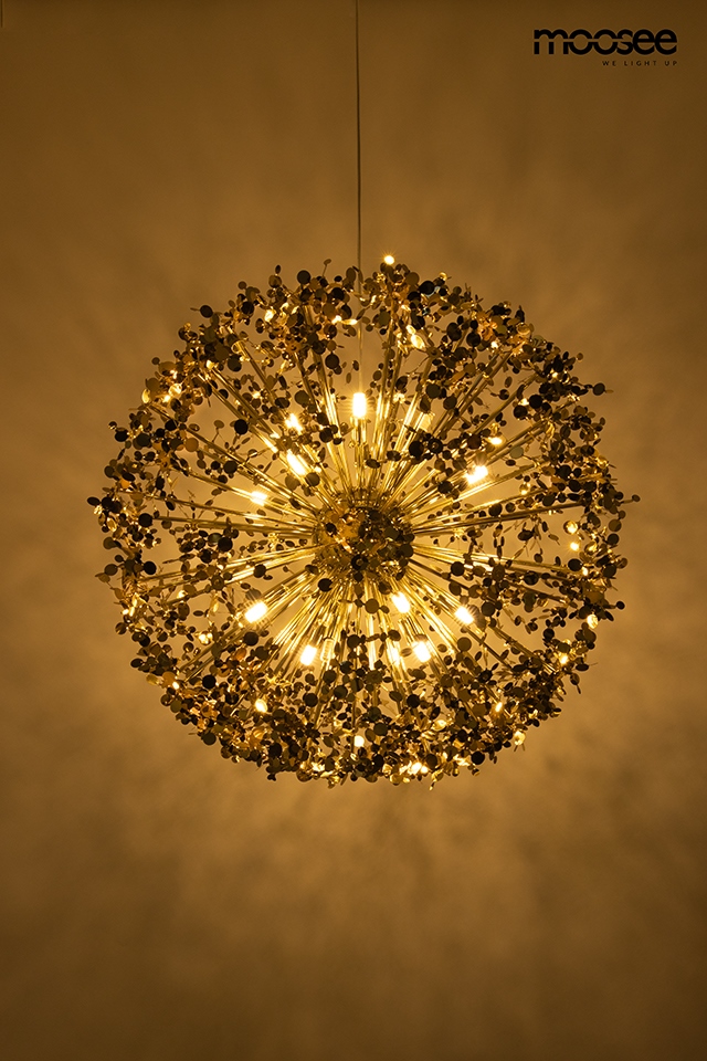 Lampa wisząca Monete 50 z 12 źródłami światła G9, w złotym kolorze. Okrągła konstrukcja z dekoracyjnymi elementami, emitująca ciepłe światło, zawieszona na cienkim przewodzie. Tło jasne, podkreślające efekt świetlny.