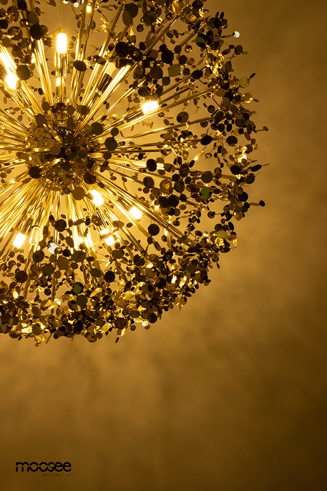 Lampa wisząca Monete 50 w kolorze złotym z 12 gniazdami G9. Ujęcie z dołu, ukazujące dekoracyjne, okrągłe elementy oraz promieniujące światło, tworzące efektowne cienie na suficie. Wykonana z metalowych prętów i ozdobnych detali.