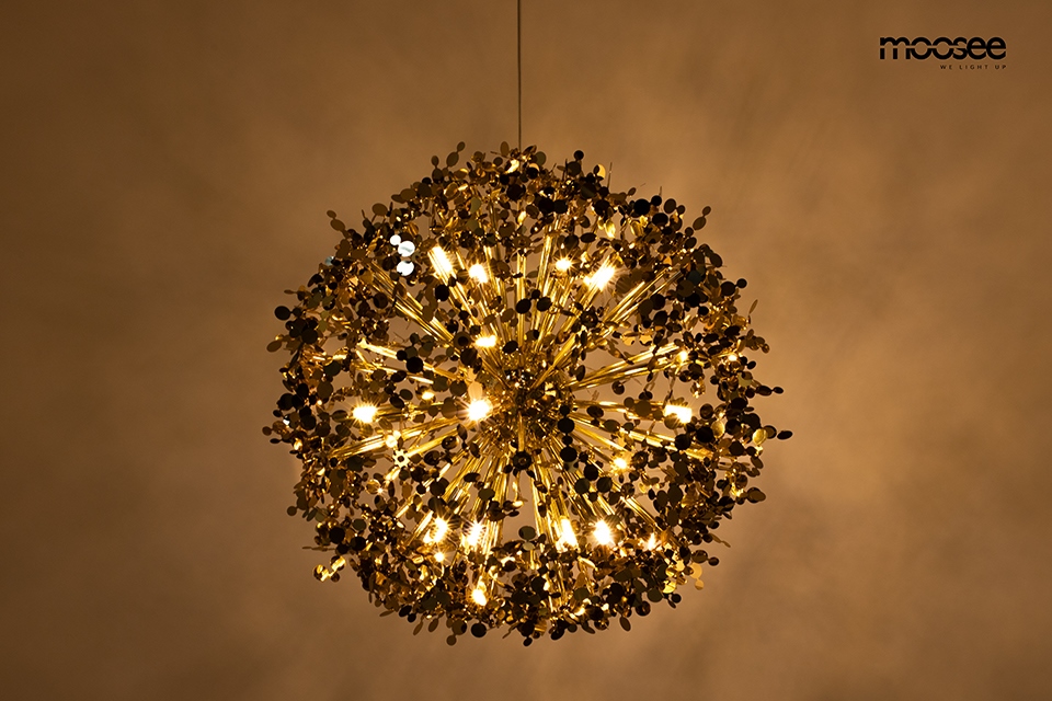 Lampa wisząca Monete 65, o złotej konstrukcji z 16 źródłami światła G9, w kształcie kulistej, dekoracyjnej formy. Umieszczona w centralnej pozycji, emitująca ciepłe światło, z detalami w formie małych okrągłych elementów.