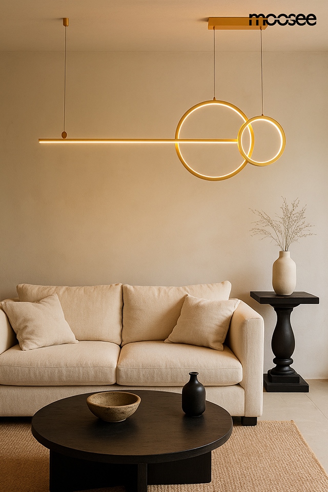 Lampa wisząca LED Rage 30W 3000K w złotym kolorze, zawieszona nad okrągłym stolikiem, składa się z prostokątnej i okrągłej formy. Tło neutralne, w aranżacji z jasnym narożnikiem oraz czarnym stolikiem i dekoracjami.