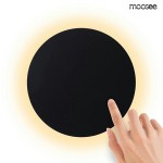 Kinkiet LED Shadow Sun 30 w kolorze czarnym, o okrągłym kształcie. Widoczna ręka dotykająca powierzchni lampy, która emituje ciepłe światło (3000K). Proste tło, podkreślające minimalistyczny design.