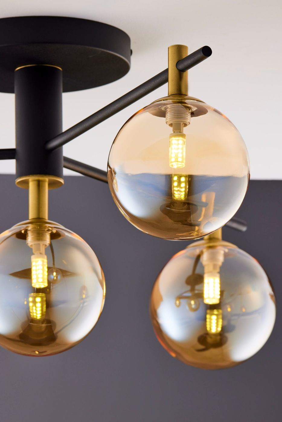 Lampa sufitowa Figaro 4xG9 w kolorze czarnym z bursztynowymi kloszami. Konstrukcja z metalowych prętów, z widocznymi żarówkami LED. Ujęcie z góry, pokazujące detale kloszy i mocowania. Tło w odcieniu szarości.