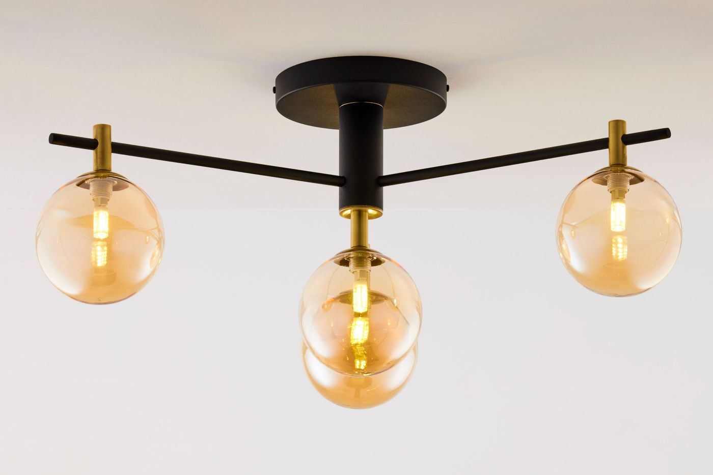 Lampa sufitowa Figaro z czarnym metalowym korpusem, z czterema bursztynowymi kloszami w kształcie kul. Ułożona poziomo, z widocznymi złotymi akcentami, zamocowana na okrągłej podstawie. Idealna do nowoczesnych wnętrz.