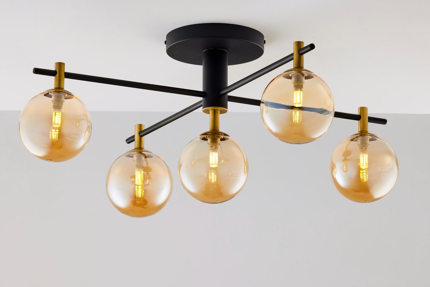 Lampa sufitowa Figaro z pięcioma oprawami G9, czarna konstrukcja z metalowymi detalami w kolorze mosiądzu. Szklane klosze w bursztynowym odcieniu, umieszczone na poziomych ramionach. Ujęcie z dołu, pokazujące całość lampy na jednolitym tle.