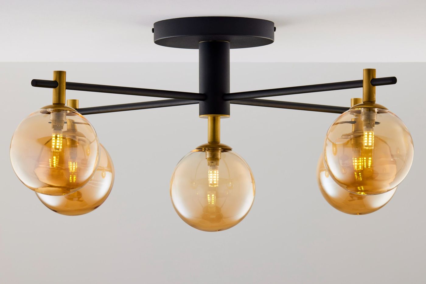 Lampa sufitowa Figaro z pięcioma kloszami G9, czarna konstrukcja z metalowymi złotymi akcentami. Klosze w kolorze bursztynowym, okrągłe, wiszące na czarnych ramionach, zamontowana na suficie. Prosta aranżacja na jasnym tle.
