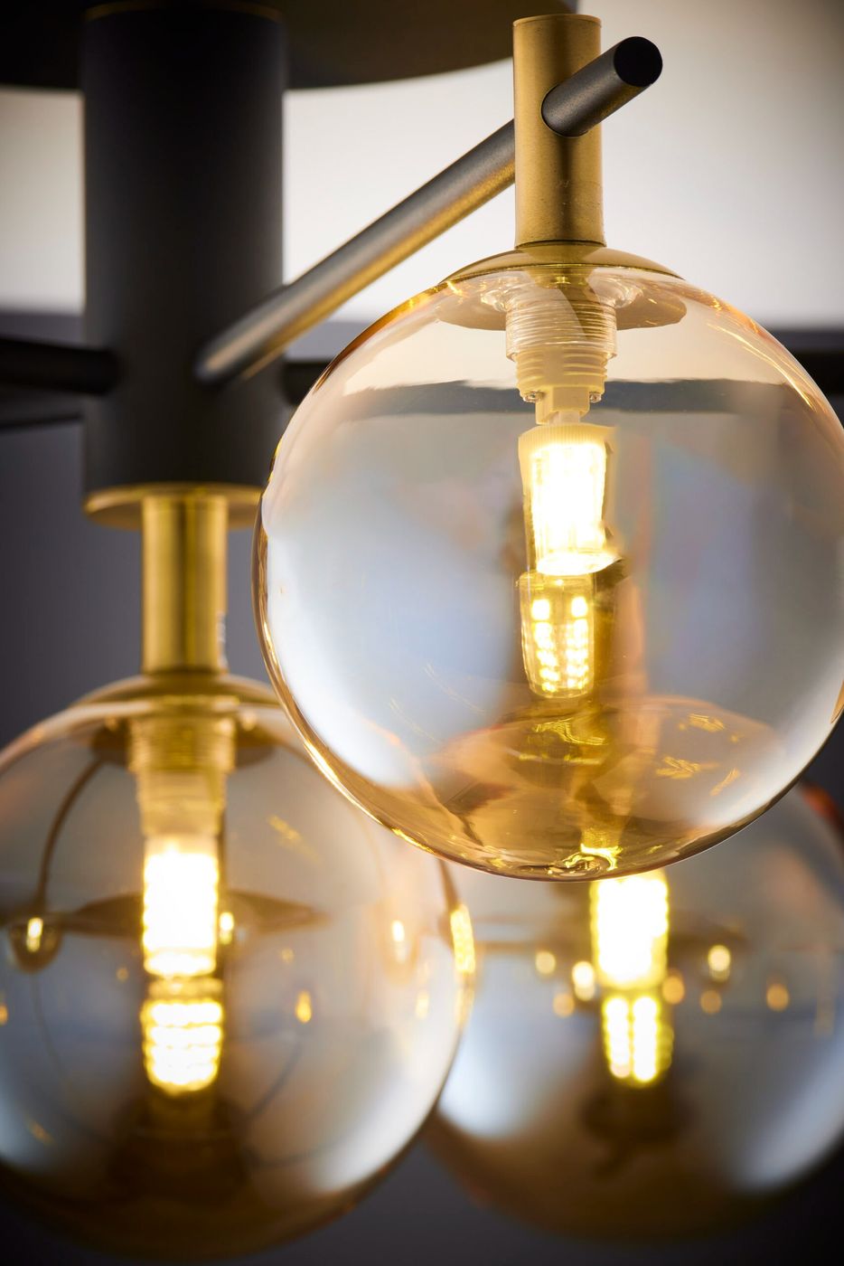 Lampa sufitowa Figaro w kolorze czarnym z sześcioma bursztynowymi kloszami, stylizowana na nowoczesną. Widoczne żarówki G9 w transparentnych kulistych kloszach, metalowe elementy w kolorze złotym. Ujęcie z bliska, skupione na detalach kloszy i żarówek.