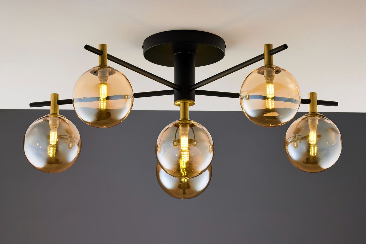 Lampa sufitowa Figaro w kolorze czarnym z sześcioma bursztynowymi kloszami. Klosze mają okrągły kształt, a całość jest zamontowana na metalowej konstrukcji z mosiężnymi detalami. Ujęcie z dołu, ukazujące wszystkie źródła światła.