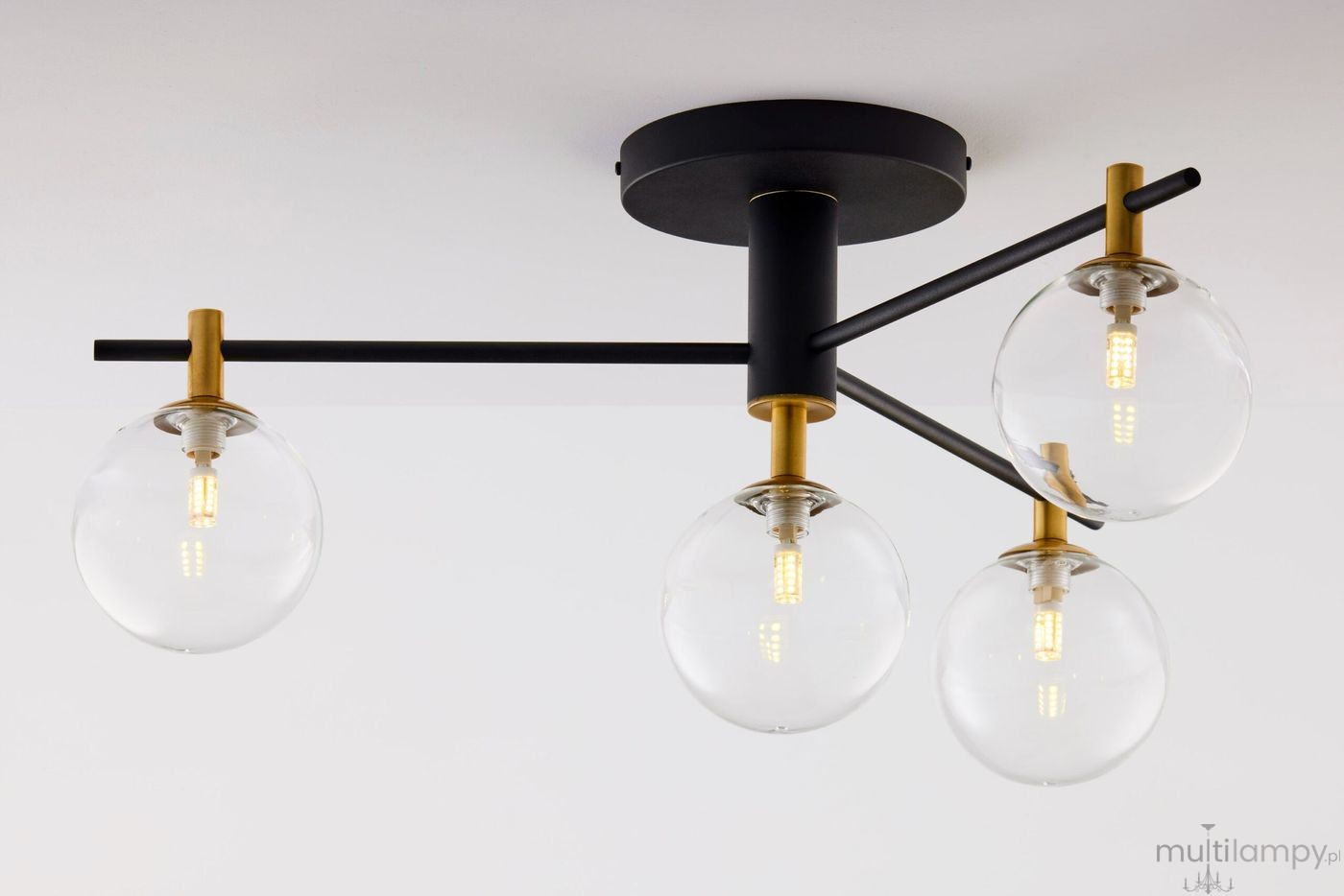 Lampa sufitowa Figaro z czarnym metalowym stelażem, wyposażona w cztery transparentne kuliste klosze. Każdy klosz osadzony na złotych elementach, z widocznymi źródłami światła. Ujęcie z dołu, pokazujące detale konstrukcji.