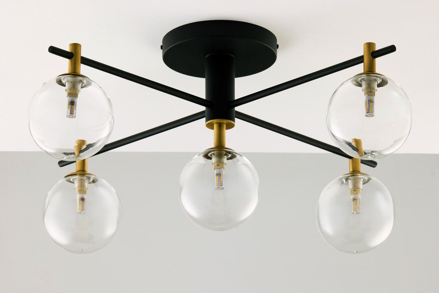 Lampa sufitowa Figaro z pięcioma gniazdami G9, czarna z elementami złotymi. Szklane, transparentne klosze w kształcie kul, umieszczone na czarnych metalowych prętach, montowane na okrągłej podstawie. Ujęcie z dołu, pokazujące strukturę i detale.
