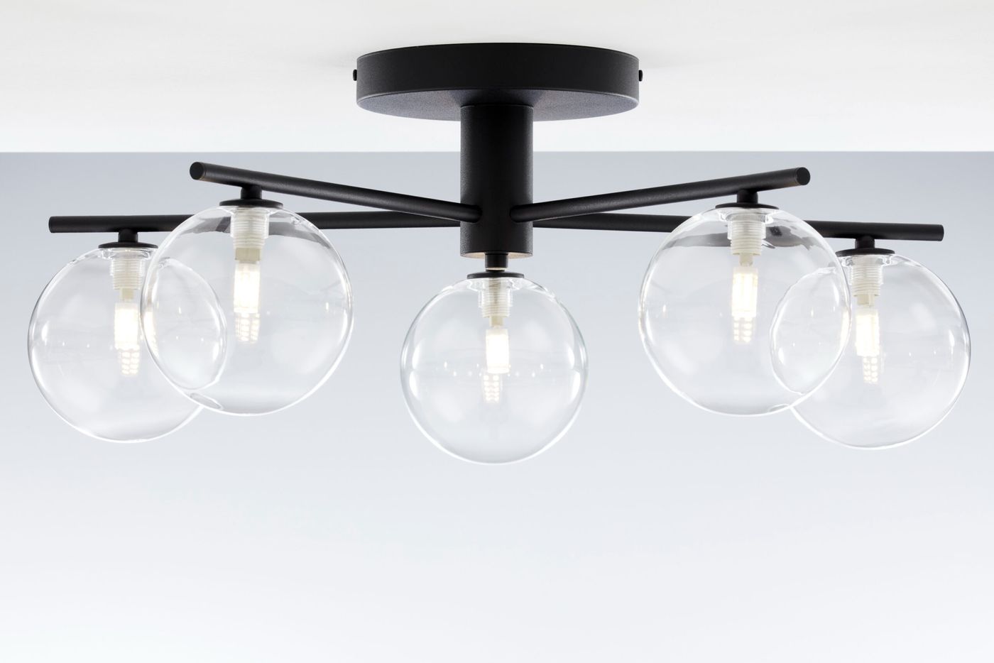 Czarna lampa sufitowa Prato z pięcioma przezroczystymi kloszami w kształcie kul. Ujęcie z dołu, ukazujące zamontowaną lampę na suficie. Widoczne źródła światła w środku kloszy, metalowa konstrukcja z prostymi liniami.