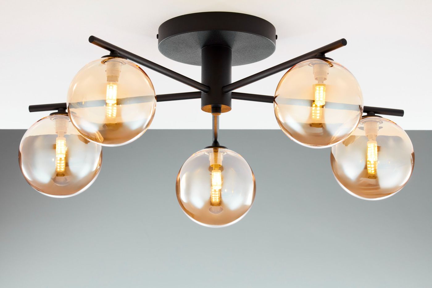 Lampa sufitowa Prato 5xG9 w kolorze czarnym z bursztynowymi kloszami. Ułożona na suficie, posiada pięć kulistych kloszy z przezroczystego szkła, które osłaniają żarówki. Metalowa konstrukcja o minimalistycznym designie, idealna do nowoczesnych wnętrz.