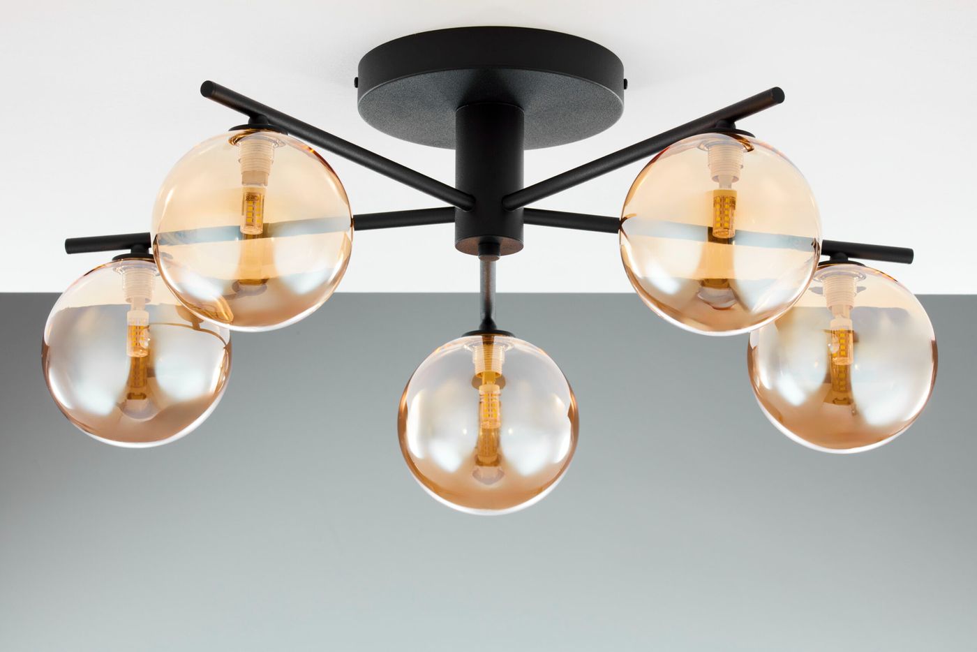 Lampa sufitowa Prato z pięcioma oprawami G9, w kolorze czarnym z bursztynowymi kloszami. Ułożona na suficie, z metalową podstawą i wyraźnymi żarówkami w każdej oprawie. Klosze mają okrągły kształt, a całość ma nowoczesny design.