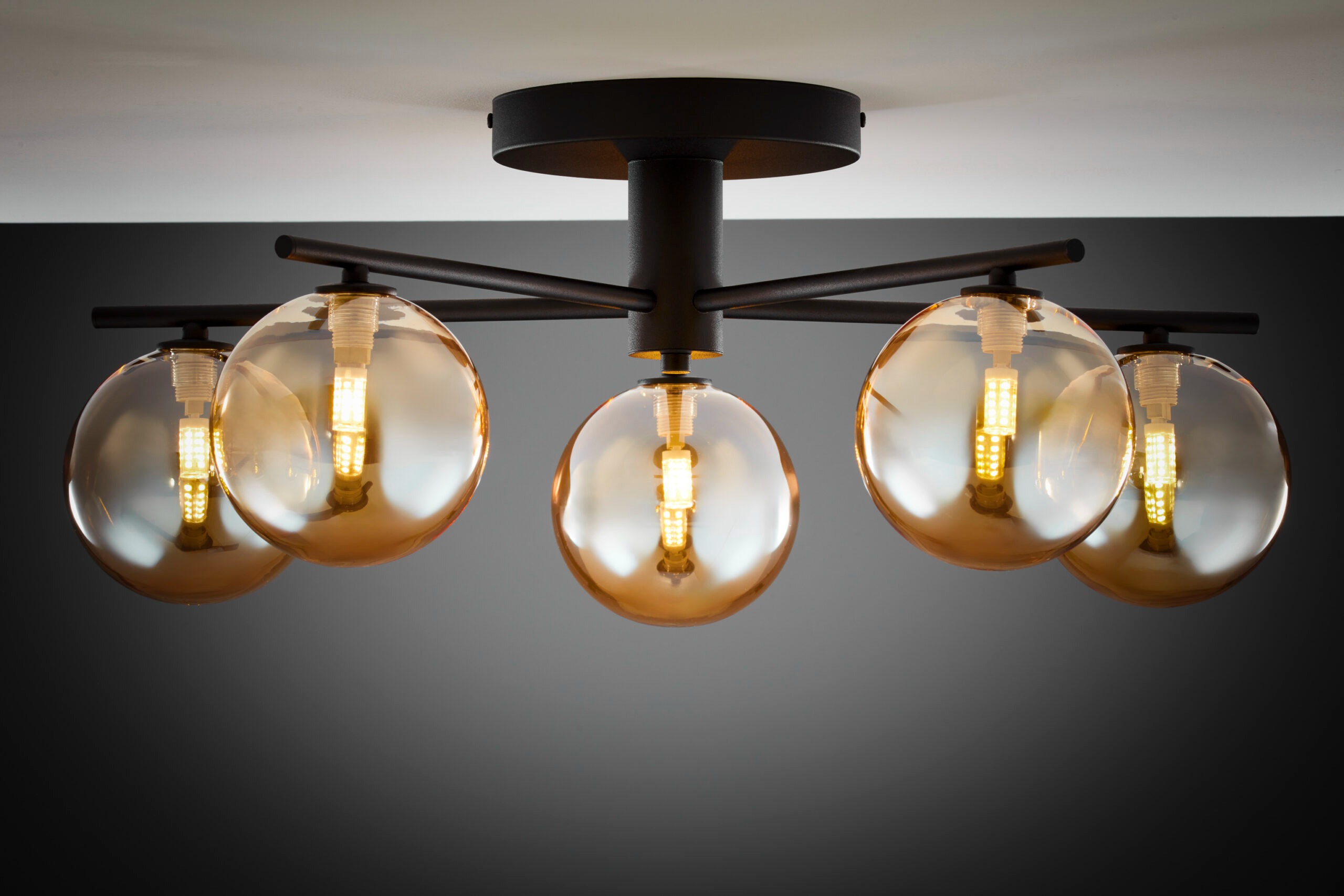 Czarna lampa sufitowa Prato z pięcioma bursztynowymi kloszami G9. Klosze mają okrągły kształt, a lampa jest zamontowana na prostym, ciemnym stelażu. Widok z dołu, ukazujący źródła światła wewnątrz kloszy.