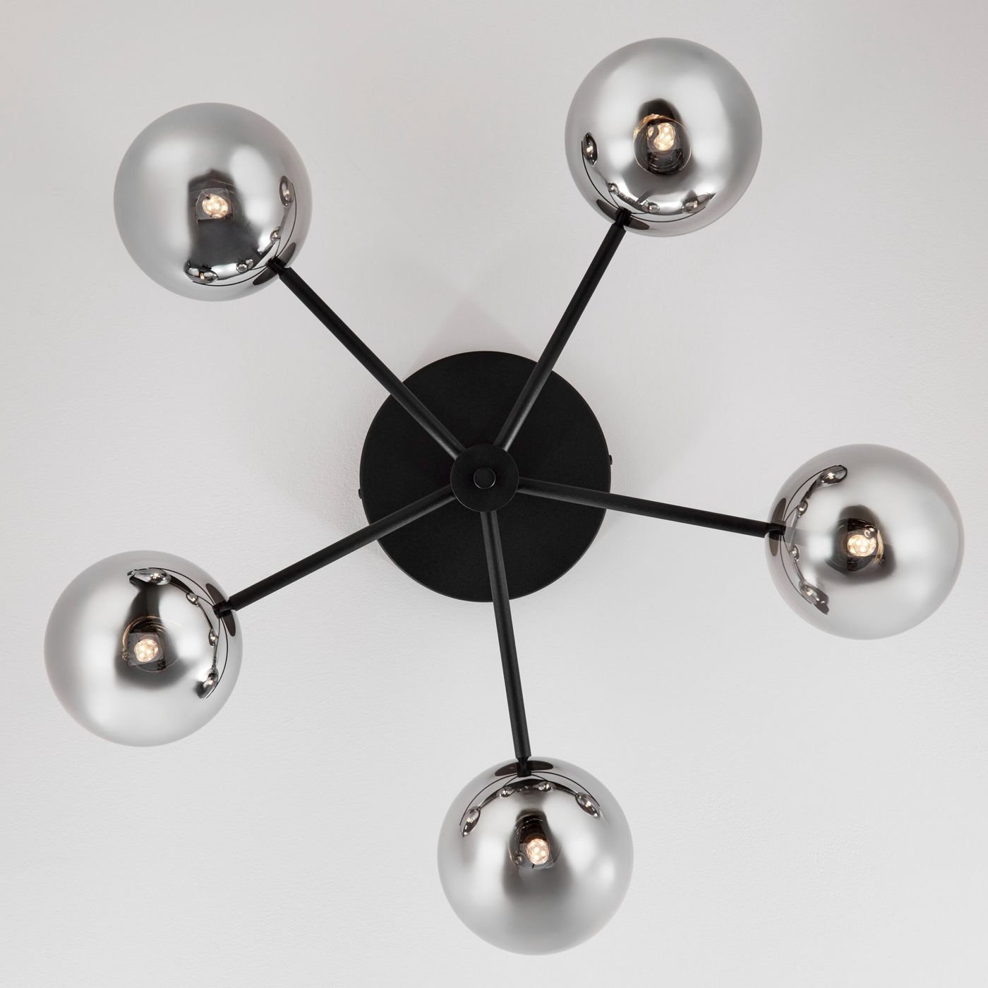 Lampa sufitowa Prato z pięcioma punktami świetlnymi G9, z czarnym metalowym stelażem i lustrzanymi, okrągłymi kloszami. Klosze umieszczone na ramionach w kształcie gwiazdy, widok z dołu.