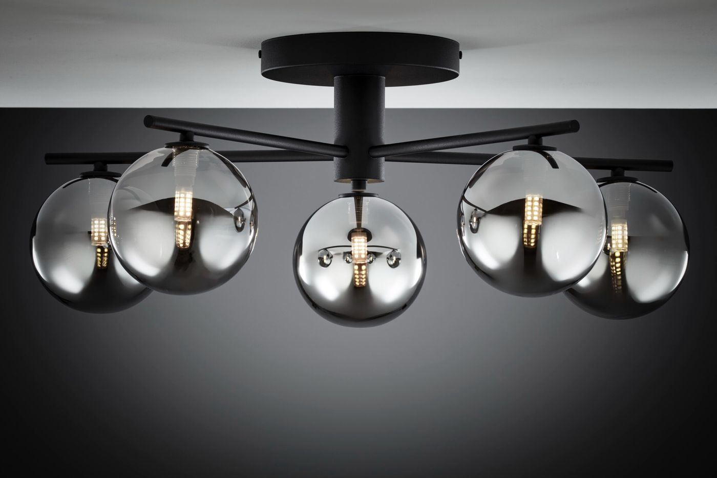 Lampa sufitowa Prato z pięcioma kulistymi kloszami w dymnym szkle, zamontowana na czarnym, metalowym stelażu. Klosze w kształcie kul, umieszczone na wysięgnikach, zapewniają nowoczesny wygląd i równomierne oświetlenie.
