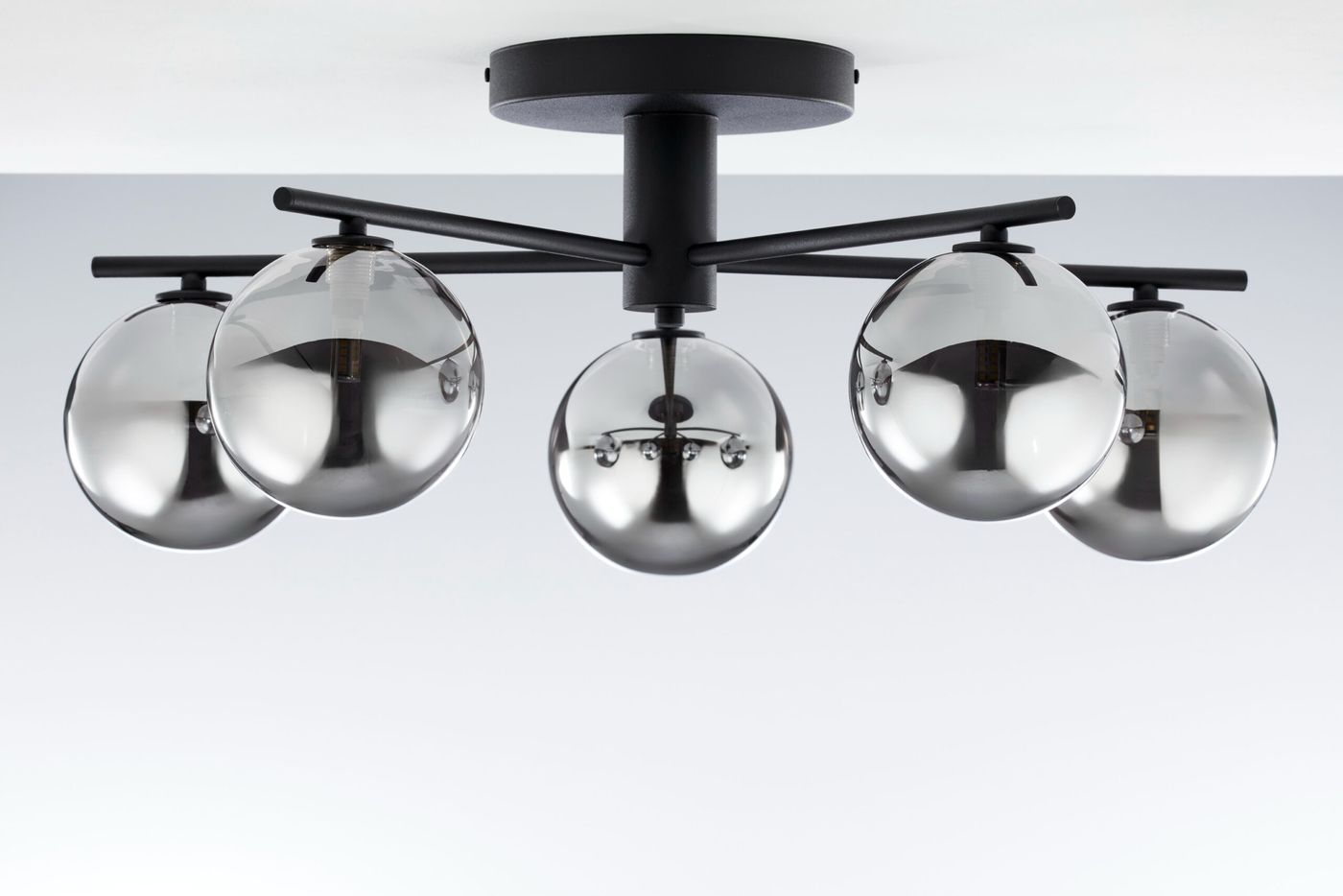 Lampa sufitowa Prato z pięcioma kloszami G9, w kolorze czarnym z dymnymi szklanymi kulami. Ujęcie z góry, wisząca konstrukcja na czarnym stelażu, z metalowymi detalami. Klosze mają zaokrąglony kształt, tworząc nowoczesny wygląd.