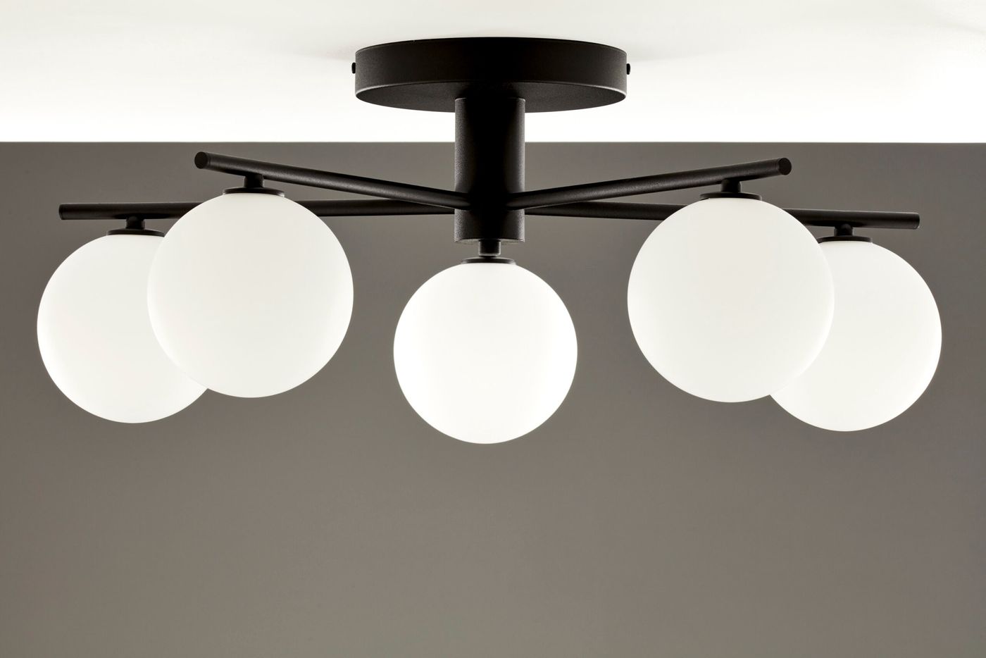 Lampa sufitowa Prato w kolorze czarnym z pięcioma białymi kulami G9. Ujęcie z dołu, pokazujące konstrukcję i kształt kloszy. Metalowy stelaż z czarnym wykończeniem, wisi pod sufitem na prostokątnej podstawie.