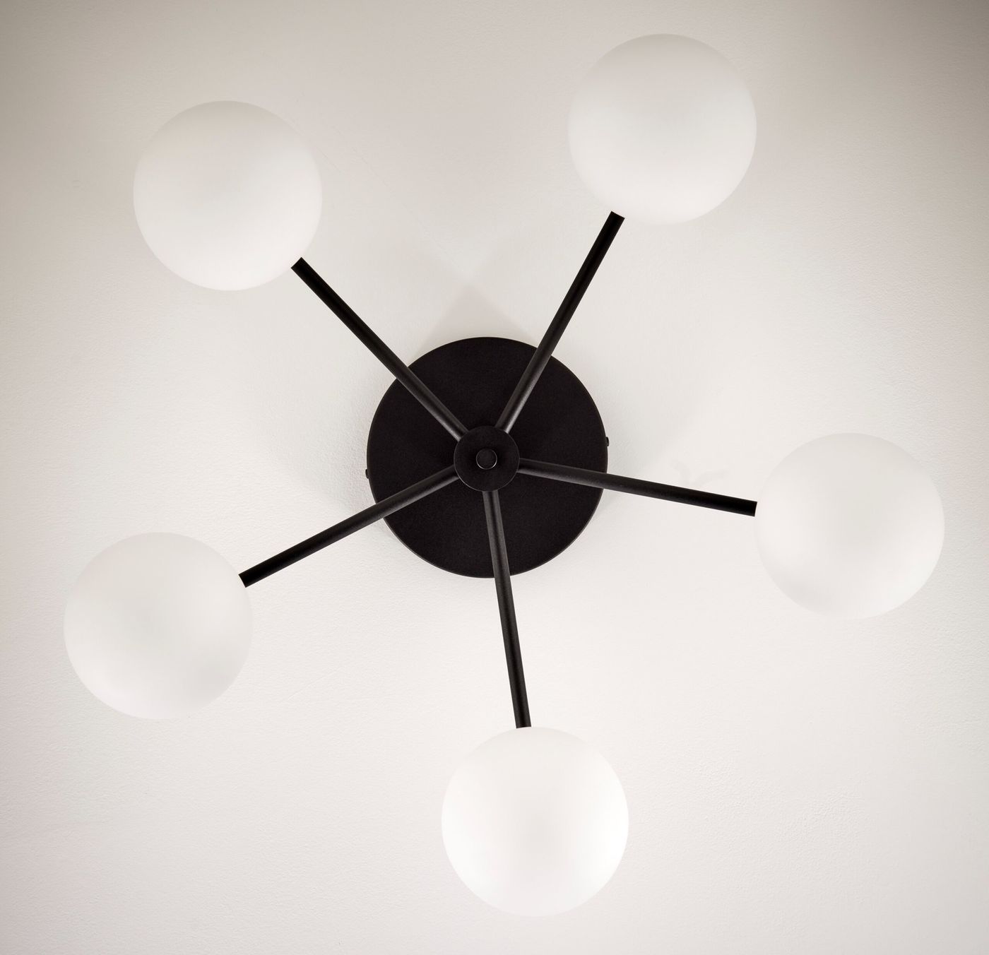 Lampa sufitowa Prato, czarna z pięcioma białymi kloszami w kształcie kul. Ujęcie z góry, ukazujące czarną podstawę oraz rozłożone ramiona. Idealna do nowoczesnych wnętrz.