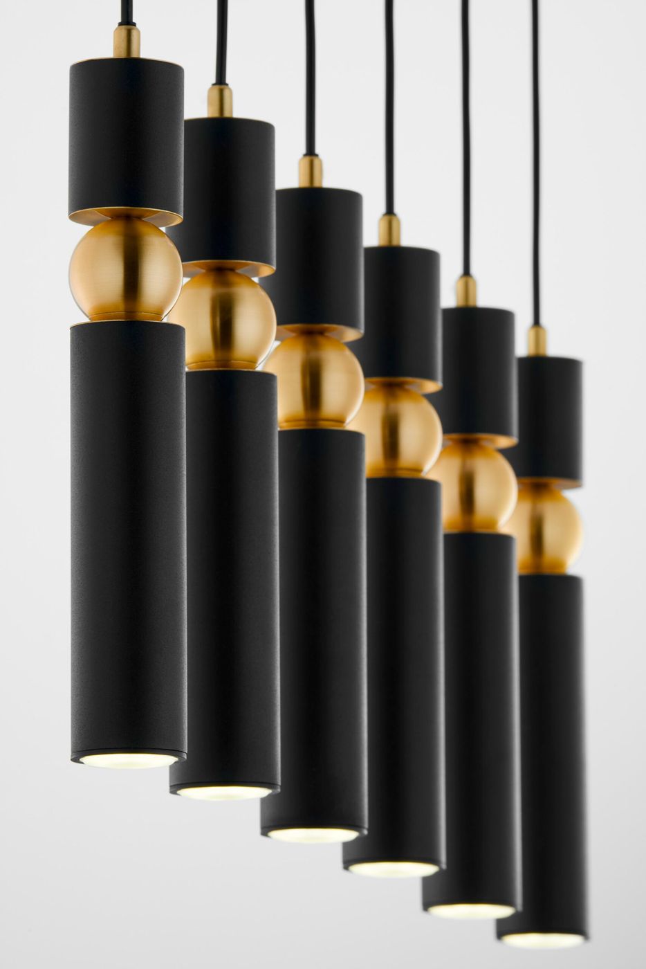 Lampa wisząca Alas z sześcioma oprawami GU10, w kolorze czarnym. Składa się z cylindrycznych elementów z matowego metalu oraz złotych kulistych detali. Produkt zawieszony na czarnych przewodach, widoczny z bliska, eksponujący nowoczesny design.