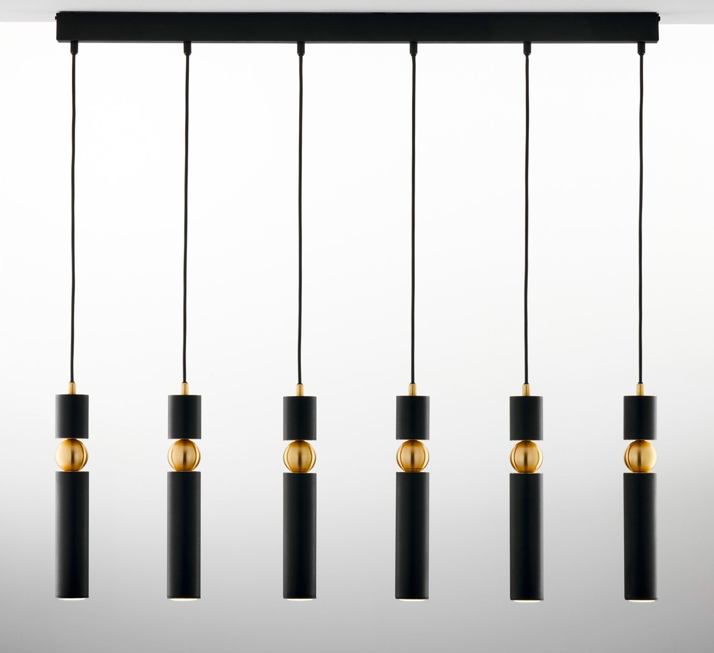 Lampa wisząca Alas w kolorze czarnym z sześcioma źródłami światła GU10. Posiada cylindryczne klosze z matowego metalu, ozdobione złotymi elementami. Zawieszona na czarnych przewodach z prostokątną podstawą.