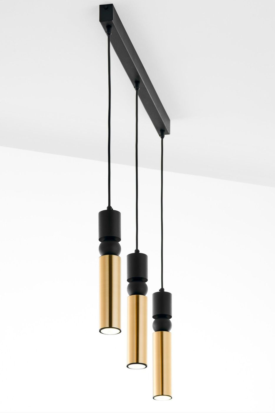 Czarna lampa wisząca Alas z trzema złotymi kloszami, zawieszona na prostokątnej, czarnej podstawie. Klosze mają cylindryczny kształt, z widocznymi detalami w postaci czarnych elementów mocujących. Idealna do nowoczesnych wnętrz.