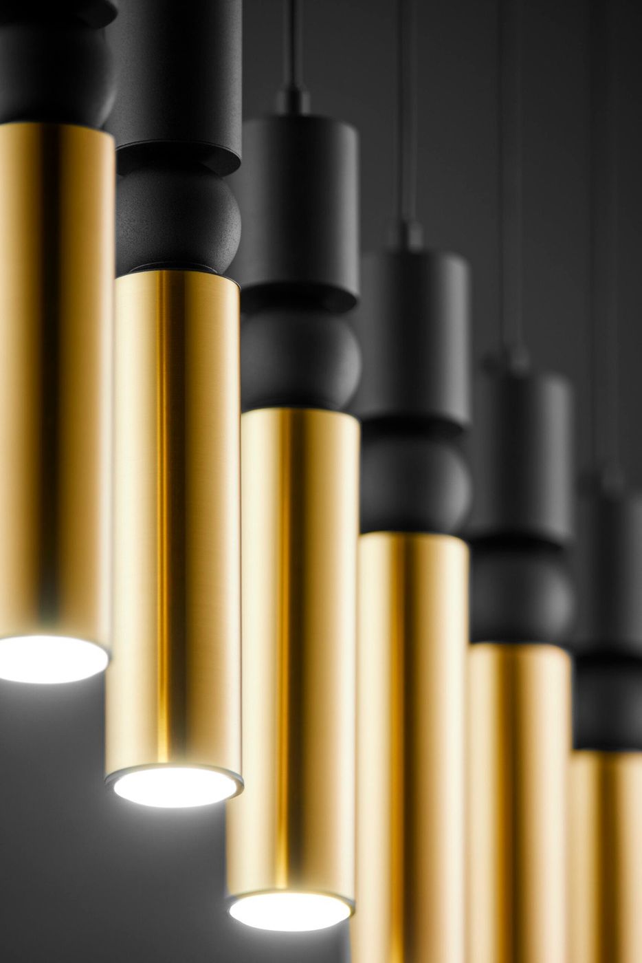 Lampa wisząca Alas w kolorze czarnym i złotym, z sześcioma oprawami na żarówki GU10. Ujęcie zbliżeniowe, ukazujące metalowe cylindry w różnych odcieniach, z detalami wykończenia. Światło skierowane w dół, zawieszona na cienkich przewodach.