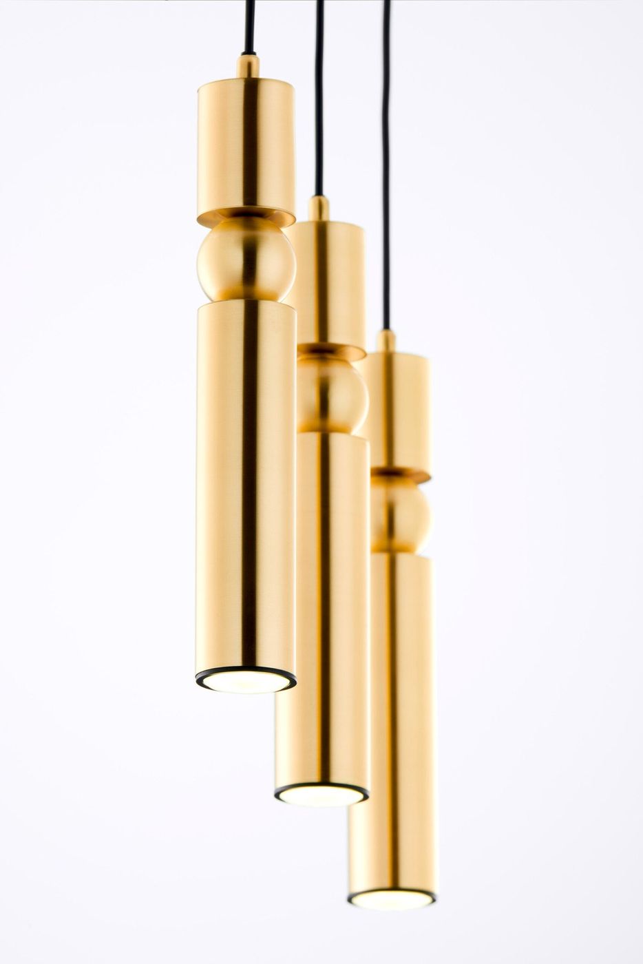 Lampa wisząca Alas z trzema źródłami światła GU10, w złotym kolorze. Słupkowata konstrukcja z matowego metalu, zawieszona na czarnych przewodach. Widoczne trzy cylindryczne klosze z otwartym dnem, umieszczone na różnych wysokościach.