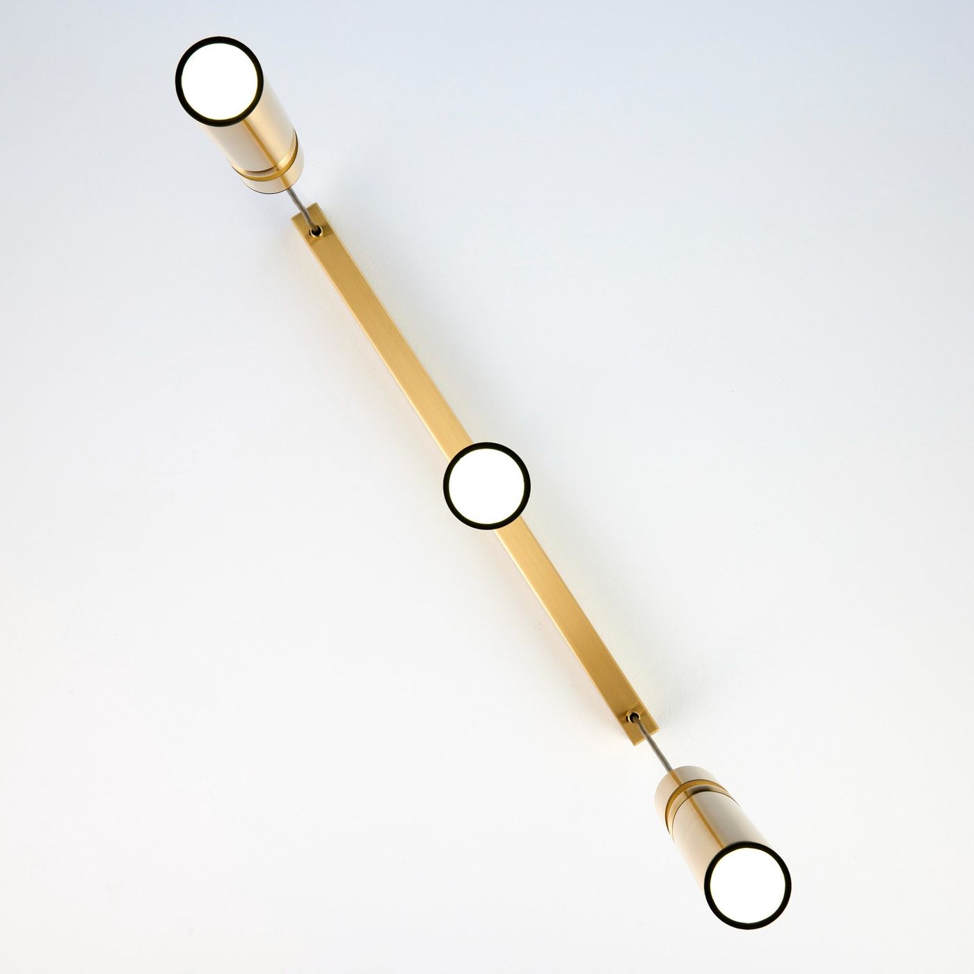 Lampa wisząca Alas w złotym kolorze z trzema oprawami na żarówki GU10. Ułożona poziomo, z cylindrycznymi kloszami i prostokątną podstawą. Tło białe, podkreślające elegancki design.