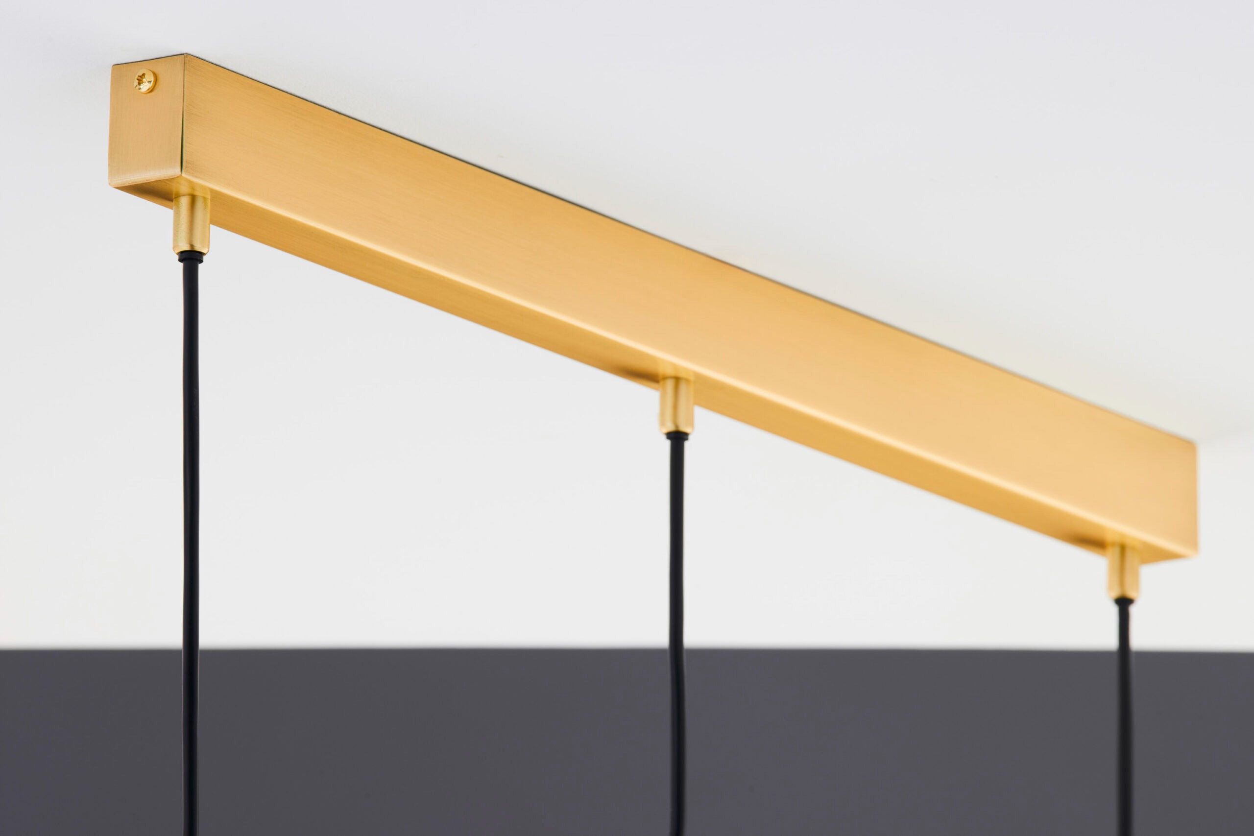 Lampa wisząca Alas w kolorze złotym, z prostokątnym metalowym kloszem, zawieszona na czarnych przewodach. Ujęcie z góry, ukazujące detale mocowania oraz minimalistyczny design. Przeznaczona do zastosowania z trzema żarówkami GU10.