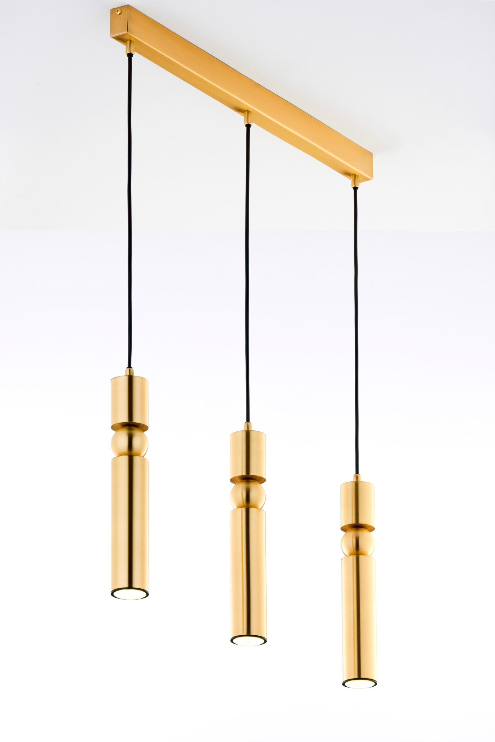 Lampa wisząca Alas w kolorze złotym, z trzema cylindrycznymi kloszami na czarnych przewodach. Ułożona poziomo, zawieszona na prostokątnej podstawie. Klosze mają różne wysokości, co tworzy dynamiczny efekt.