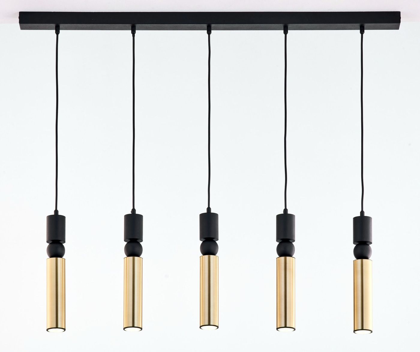 Lampa wisząca Alas z pięcioma oprawami na żarówki GU10 w kolorze czarnym i złotym. Produkt zawieszony na prostokątnej, czarnej podstawie, z długimi, czarnymi przewodami. Wysokie, cylindryczne klosze w złotym odcieniu.