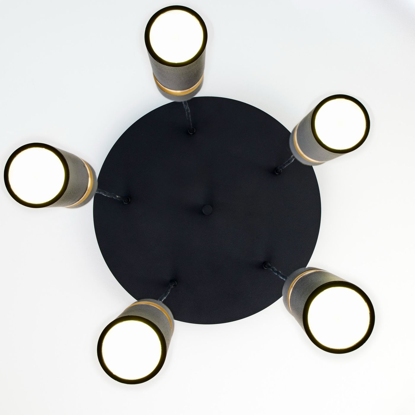 Lampa wisząca Alas z pięcioma oprawami GU10, czarna, z okrągłą podstawą. Wyposażona w cylindryczne klosze z metalicznymi detalami, montowana sufitowo, widok z dołu, na białym tle.