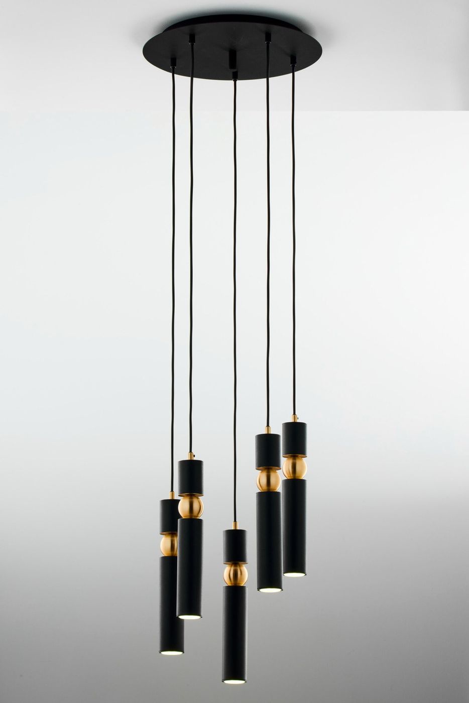 Lampa wisząca Alas z pięcioma źródłami światła GU10, w kolorze czarnym z elementami złotymi. Prosta, cylindryczna forma, zawieszona na cienkich linkach. Kąt ujęcia z góry, na jednolitym tle.