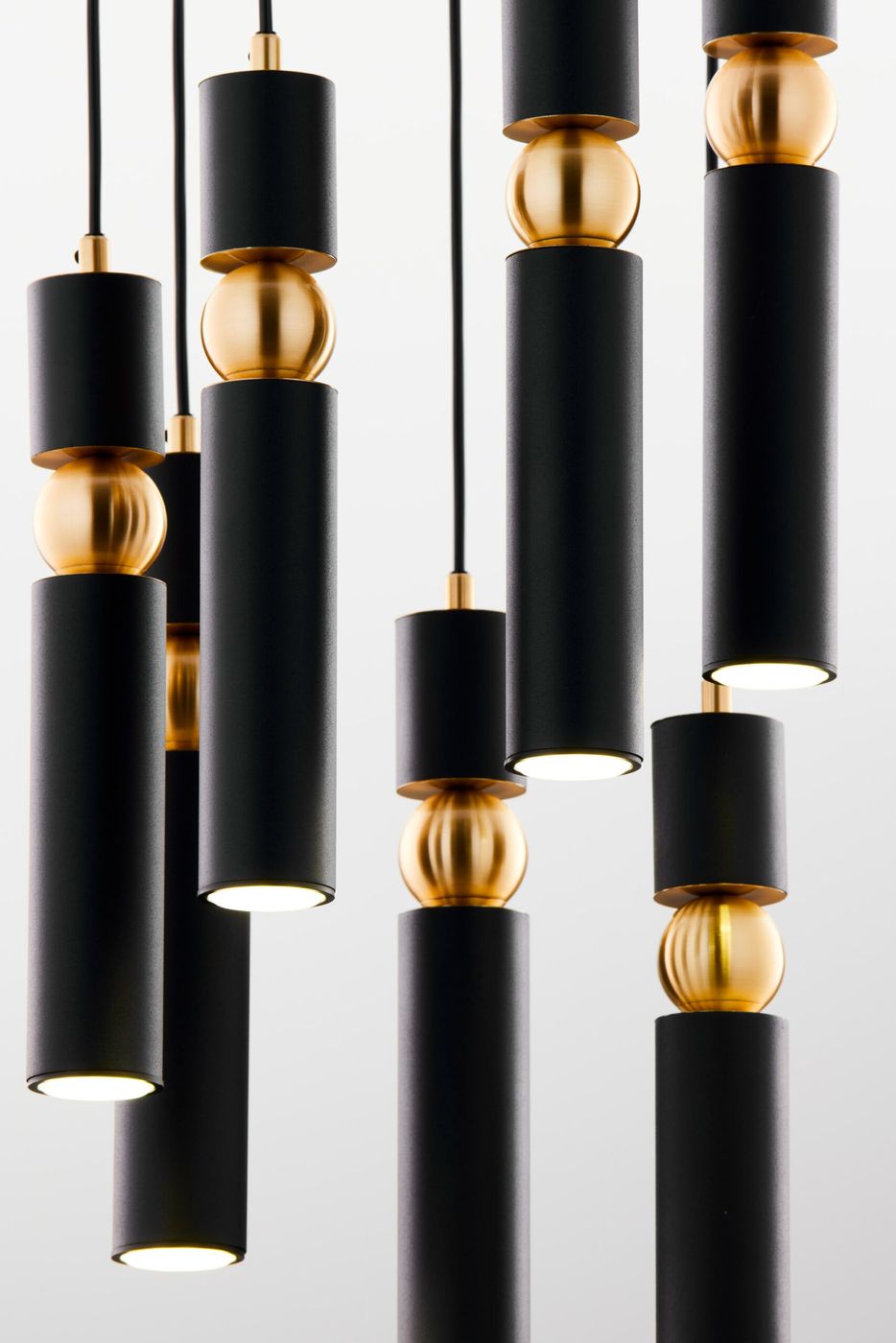 Lampa wisząca Alas w kolorze czarnym z siedmioma oprawkami GU10. Składa się z cylindrów o matowej fakturze oraz złotych kul, zawieszonych na czarnych przewodach. Produkt w zbliżeniu, ukazujący detale i konstrukcję.