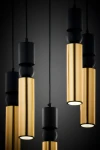 Lampa wisząca Alas z pięcioma oprawami GU10. Czarne elementy metalowe i złote cylindryczne klosze. Klosze zawieszone na cienkich przewodach w kształcie prostokątów, w różnej wysokości. Tło ciemne, podkreślające elegancki design lampy.