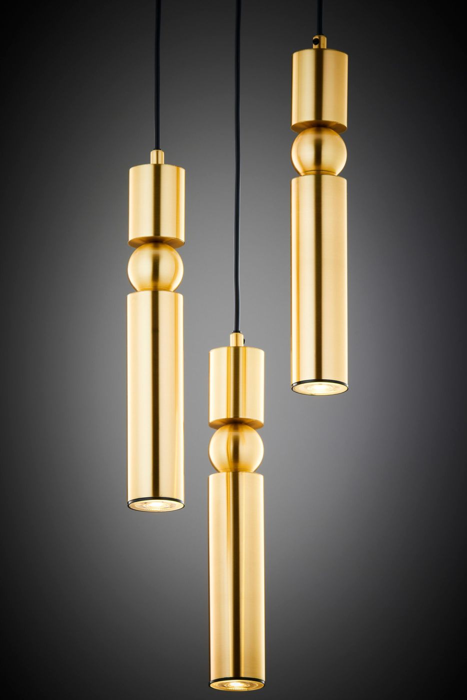 Lampa wisząca Alas w kolorze złotym z trzema źródłami światła GU10. Składa się z trzech cylindrycznych elementów o różnych wysokościach, z połyskującą powierzchnią, zawieszonych na czarnym kablu.