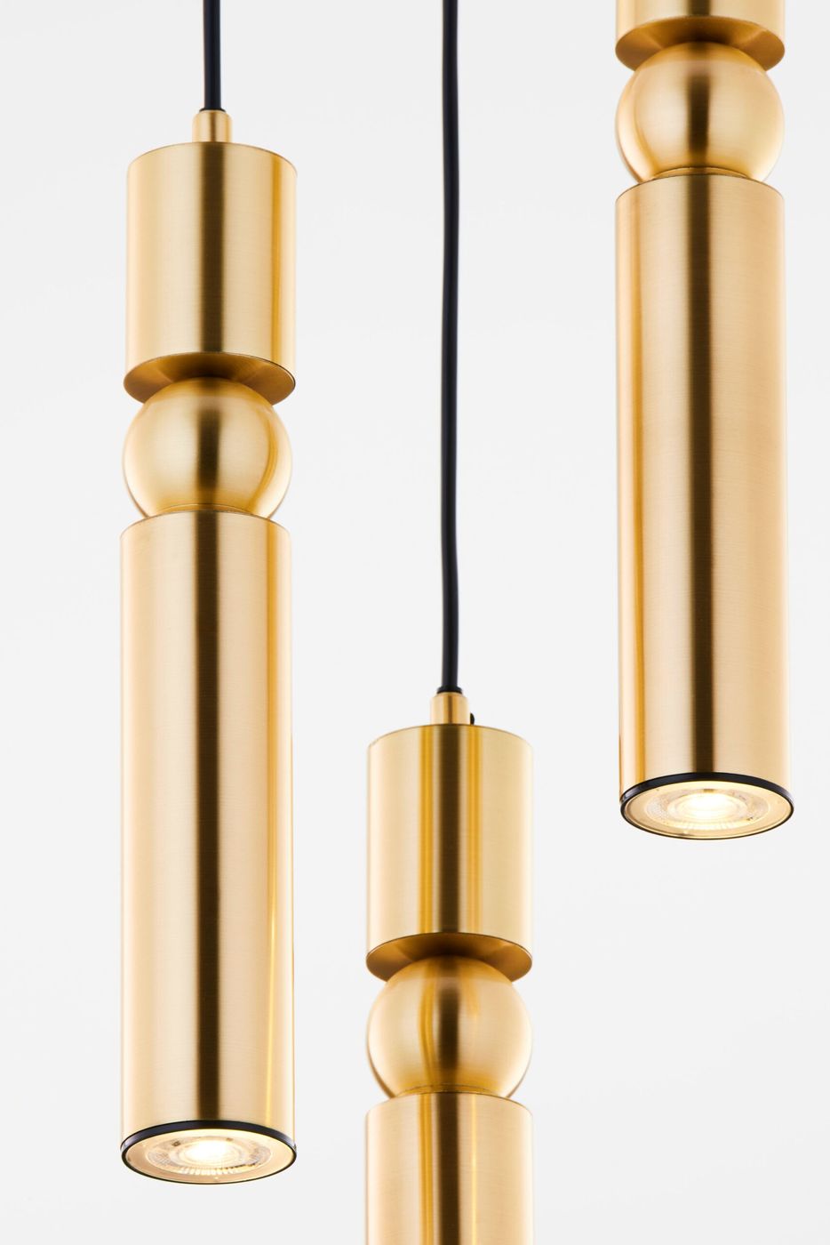 Lampa wisząca Alas w kolorze złotym, składająca się z trzech cylindrycznych elementów o różnej długości, z czarnym przewodem. W górnej części widoczne są okrągłe detale. Całość ma nowoczesny, minimalistyczny design.