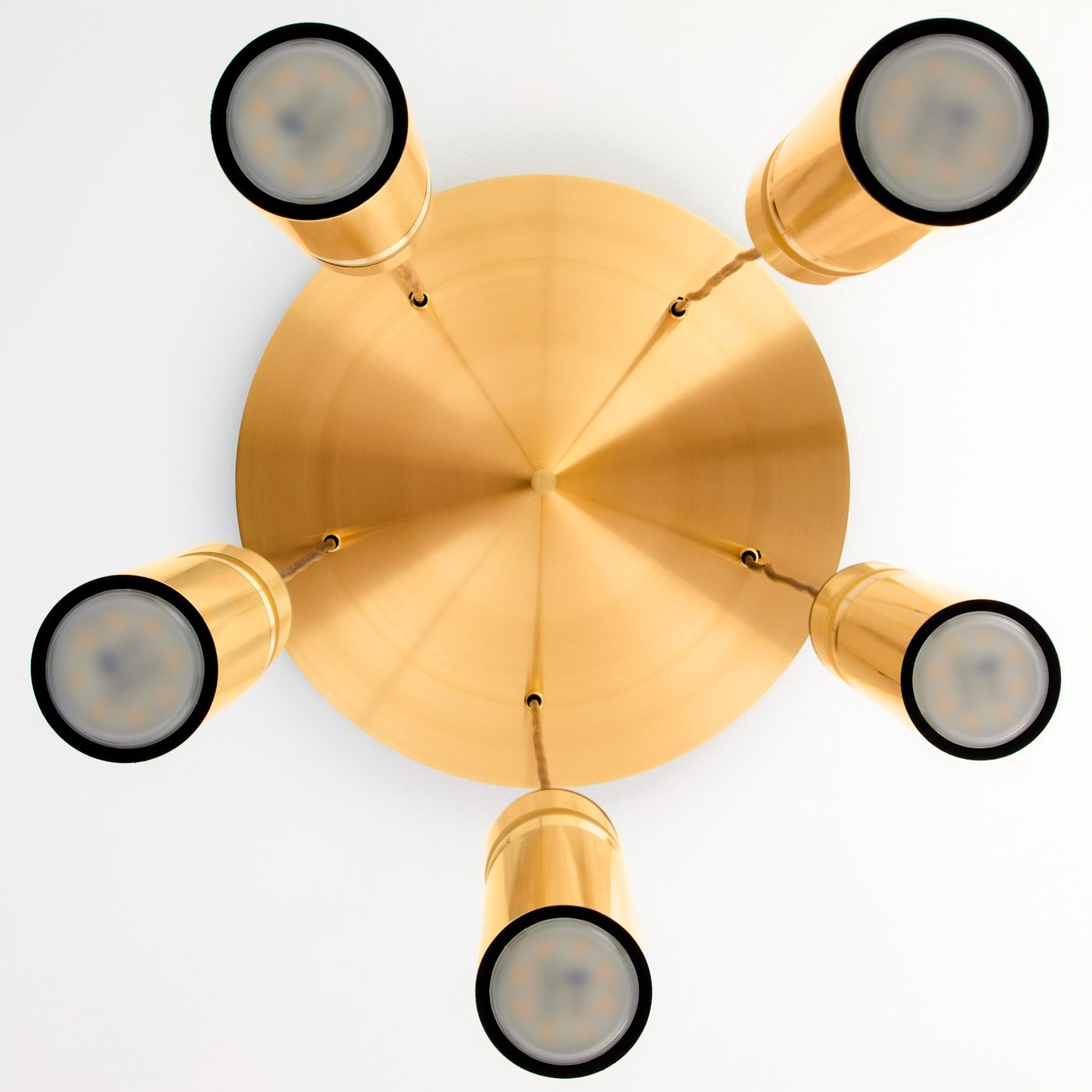 Lampa wisząca Alas w kolorze złotym z pięcioma oprawami na źródła światła GU10. Zbliżenie na okrągłą podstawę i cylindryczne klosze, umieszczone w równych odstępach, z widocznymi lekko przezroczystymi żarówkami.