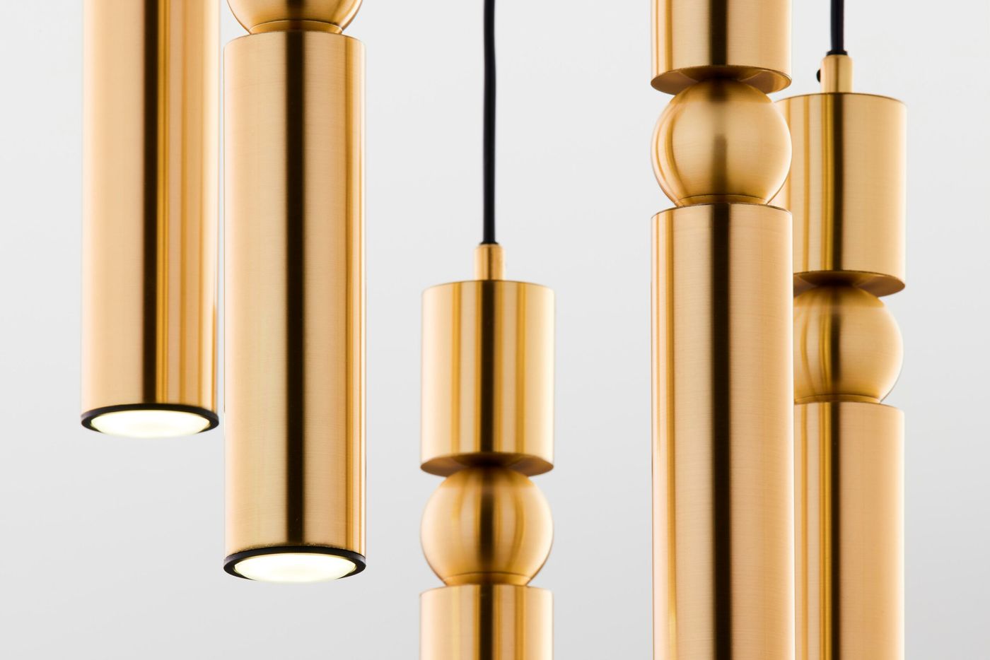 Lampa wisząca Alas w kolorze złotym, z pięcioma źródłami światła GU10. Składa się z cylindrycznych i kulistych elementów, zawieszonych na czarnym przewodzie, ukazujących nowoczesny design. Ujęcie zbliżeniowe na detale.