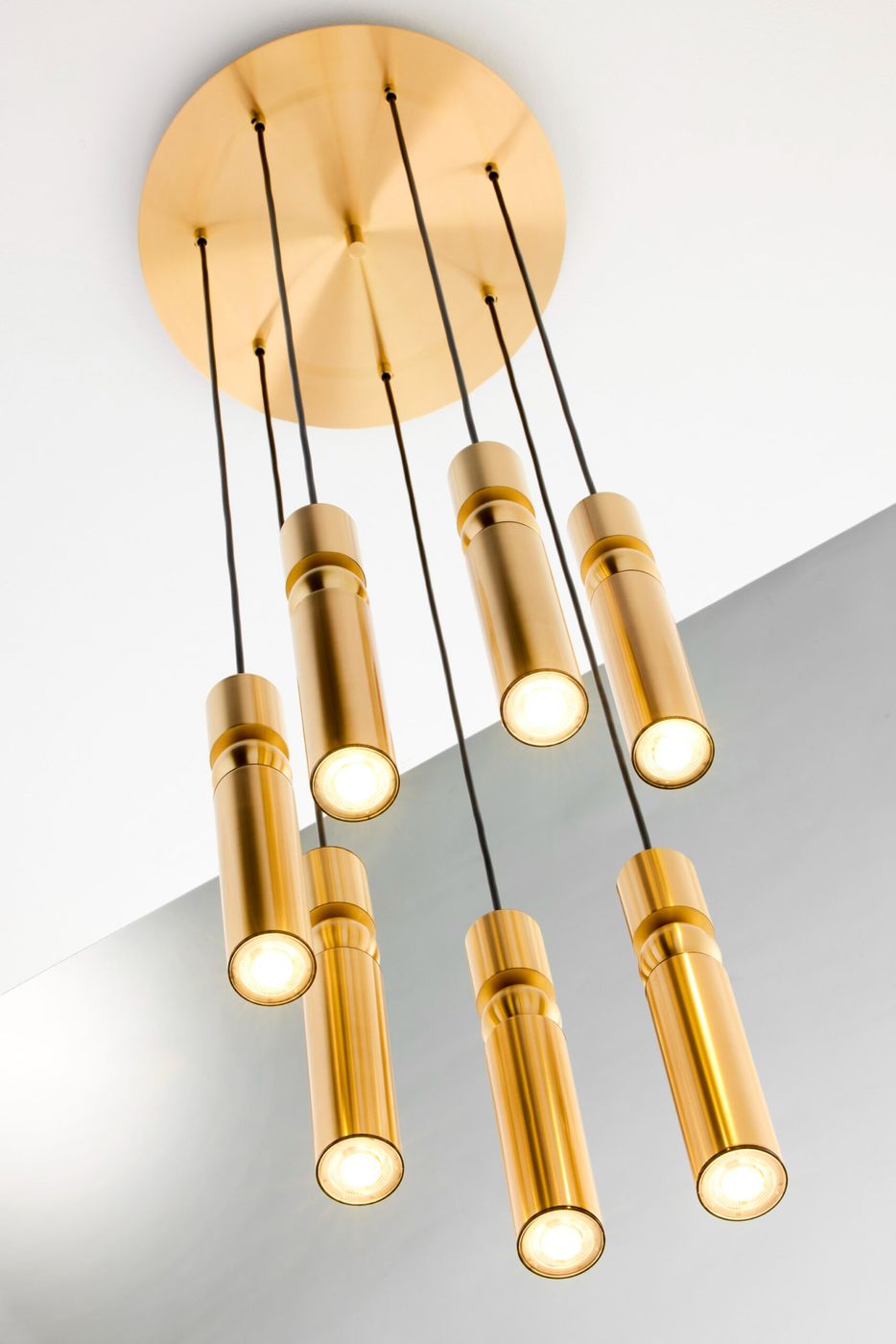 Lampa wisząca Alas z siedmioma źródłami światła GU10, w złotym kolorze. Produkt zawieszony na czarnych przewodach, z okrągłą, złotą podstawą. Klasyczny, cylindryczny kształt lamp, emitujących jasne światło.